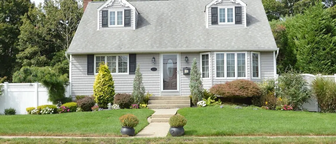 A gray Cape Cod-style house with a landscaped front yard