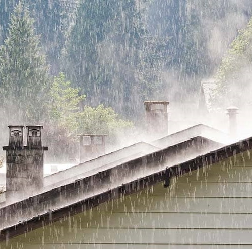 A house roof in woods under heavy rain, possibly symbolizing emergency plan for home during a natural disaster.
