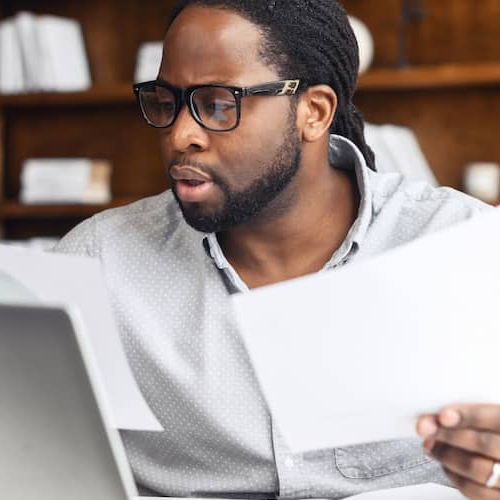 A man reviewing paperwork at a laptop, possibly managing real estate or financial documents.