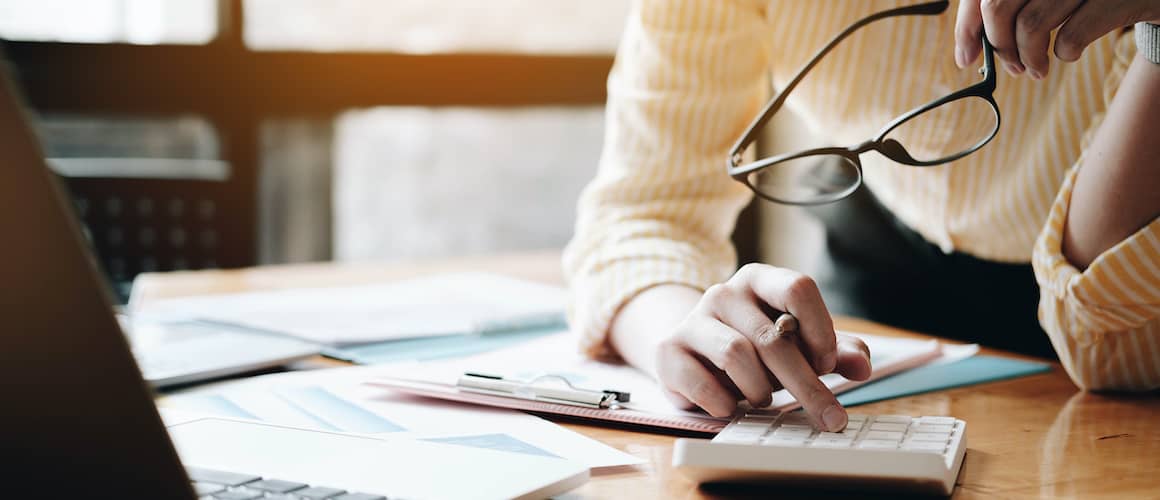 Man going over finances and using calculator with glasses hanging from mouth.