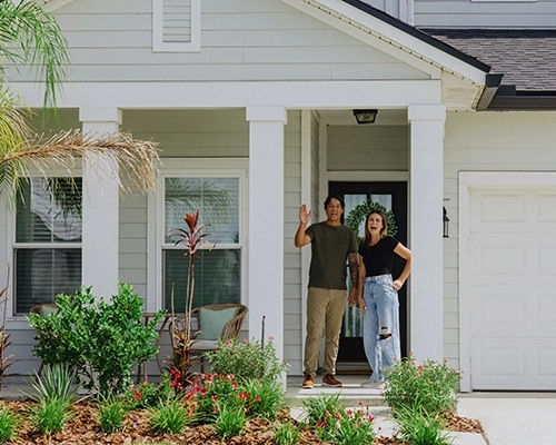 Couple smiling and waving from the door of their green pastel colored home.