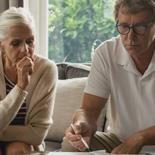 An elderly couple sitting on couch possibly calculating taxes or investments.