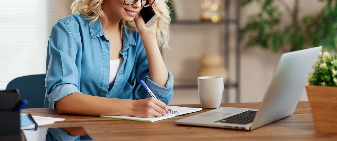 A blonde woman writing notes while on the phone, potentially related to real estate or work-related tasks.