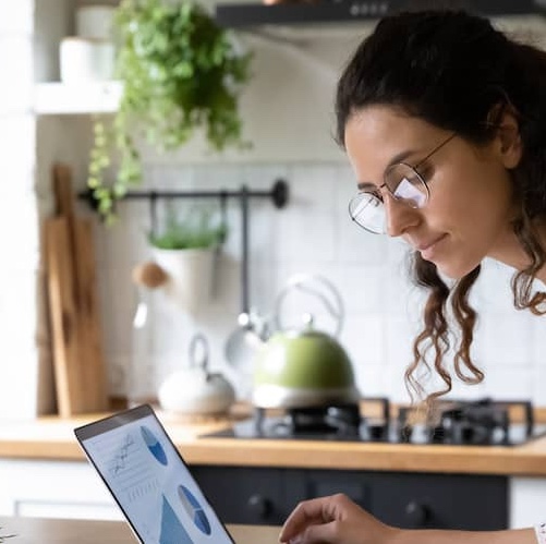 Woman reviewing financial graphs on laptop at kitchen table.