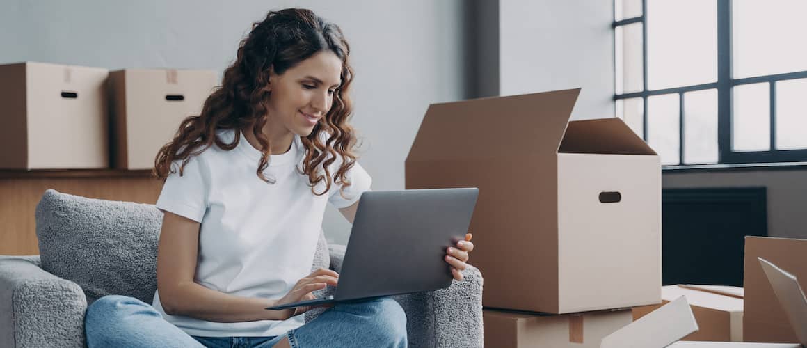 Woman surrounded by moving boxes looks for a moving company on her computer.