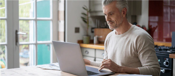 Man using a laptop on the kitchen counter at home.