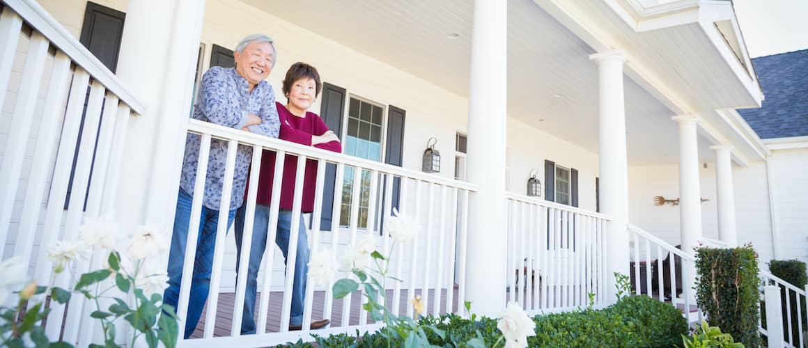 Asian couple on a front porch leaning on a railing, potentially discussing property or enjoying a home.