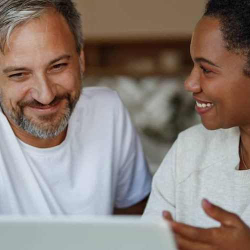 A man and a women looking at the laptop and smiling.