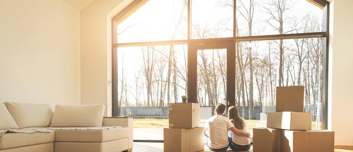 A couple enjoying sunlight in their newly bought home surrounded by cardboard boxes.