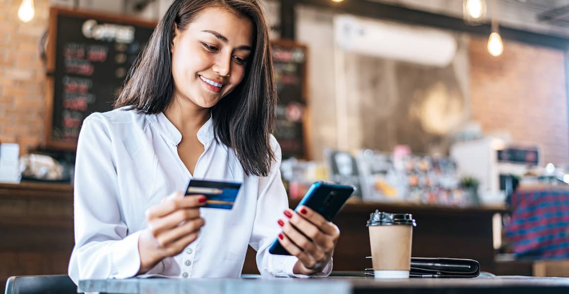 Woman at coffee shop shopping online on her phone using her credit card.