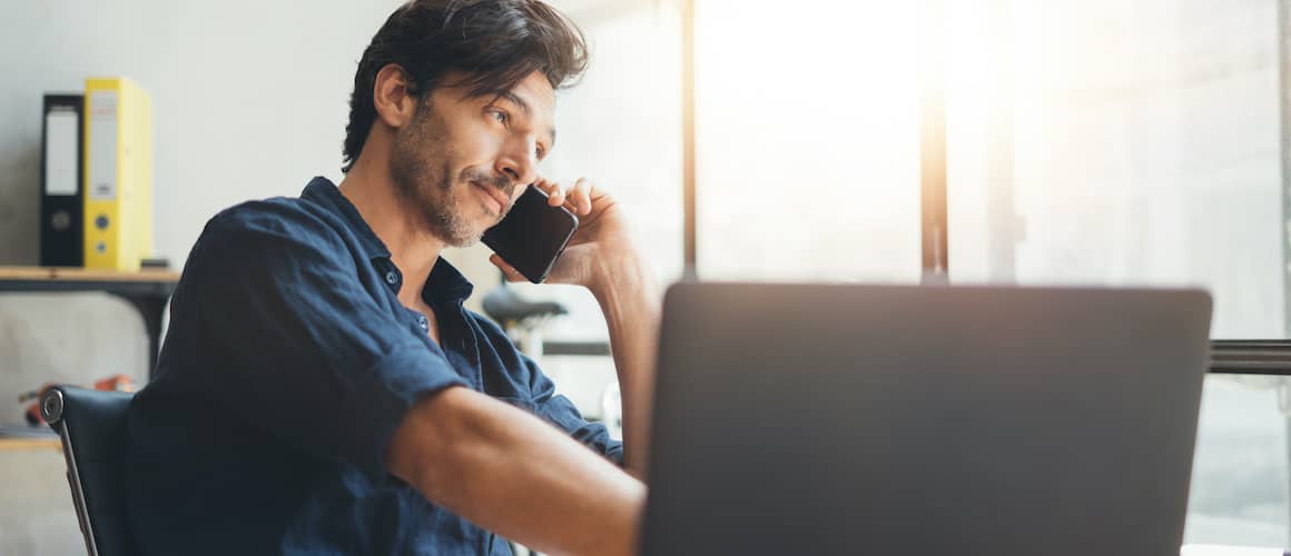 A person talking on phone while also working on his laptop.