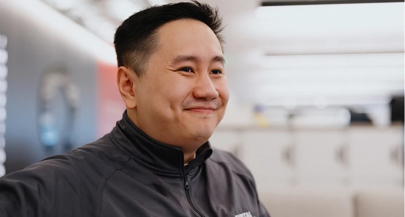 A person wearing a black shirt is indoors, standing in front of a brick wall.