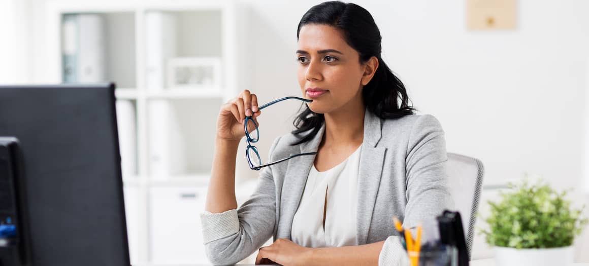 A woman thinking at a computer, suggesting contemplation or decision-making in real estate or finances.