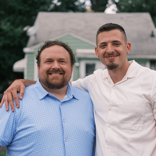 Men smiling, with one wrapping his arm around the other.