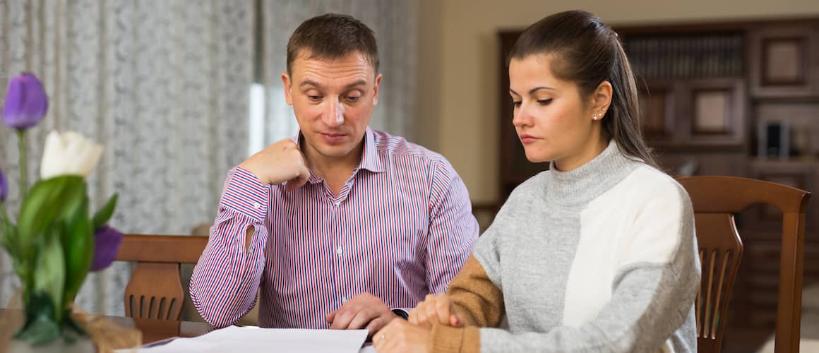 Young couple seeming pensive while looking over finances on paper at home.