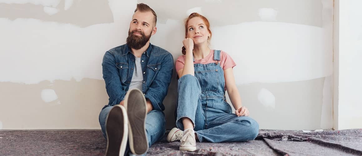A young couple sitting on the floor side by side, potentially discussing home-related decisions or planning.