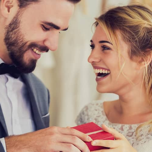 couple in wedding attire smiling and laughing holding red box