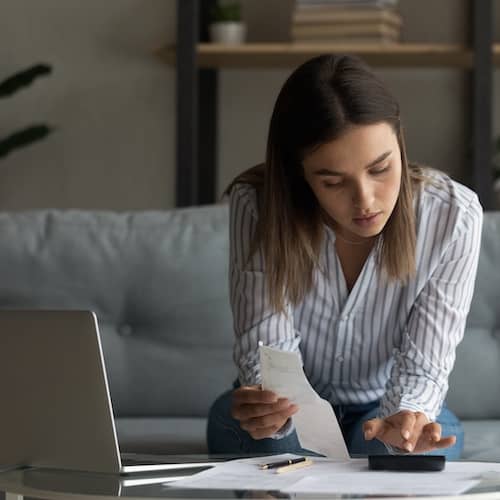 Young woman looking over her finances using a computer and calculator.