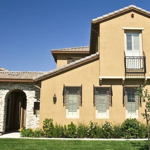 Two story tan house with green front yard in California.