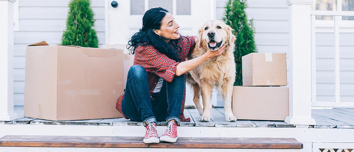 A woman petting her dog surrounded by cardboard boxes possibly indicating recent move to her new home.