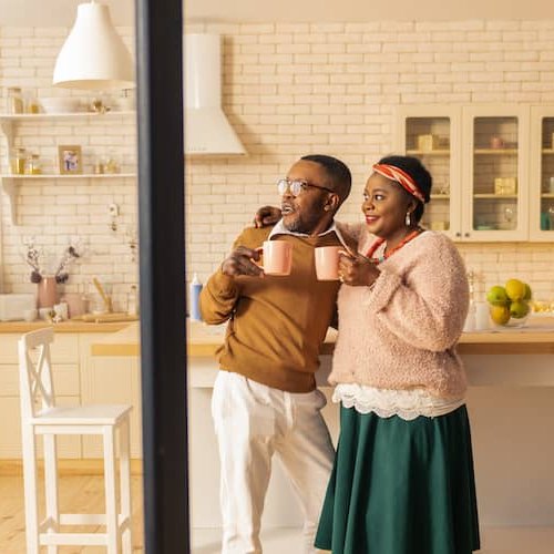 A couple having a beverage in the kitchen and looking outside the window.