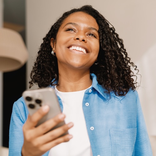 Woman smiling as she looks up from phone.