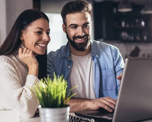 A couple engaged with a computer in their home, likely researching or managing aspects related to their property or residence.