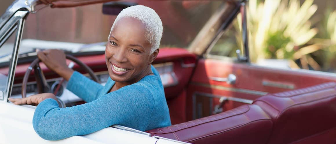 Mature African American woman in a red convertible and smiling at the camera.