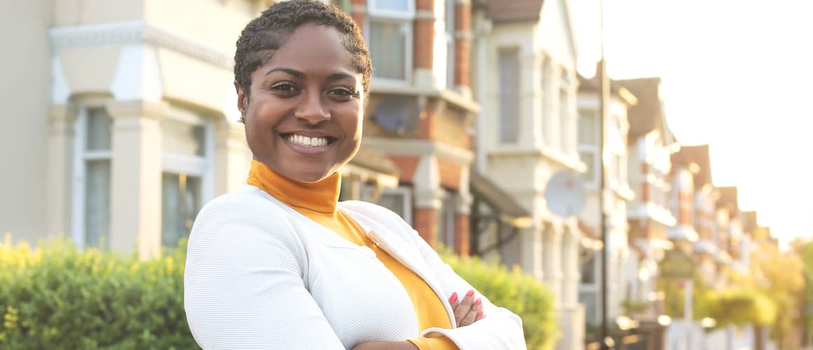 A woman standing in front of a row of houses, showcasing a peaceful neighborhood setting.