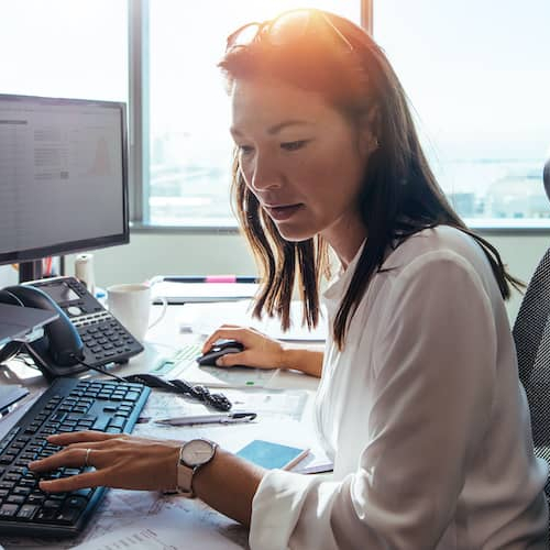 Professional woman typing something with multiple screens in front of her.