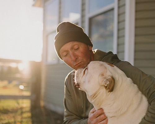 Man and large dog sitting on porch staring at each other.