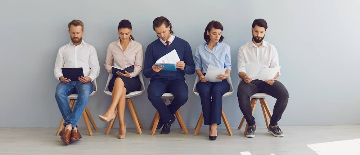 Line of people waiting for a job interview while sitting in chairs.