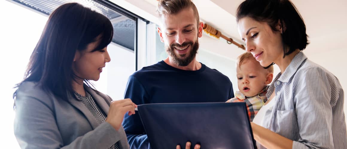 Couple holding baby looking at a document in a folder a realtor is holding up.