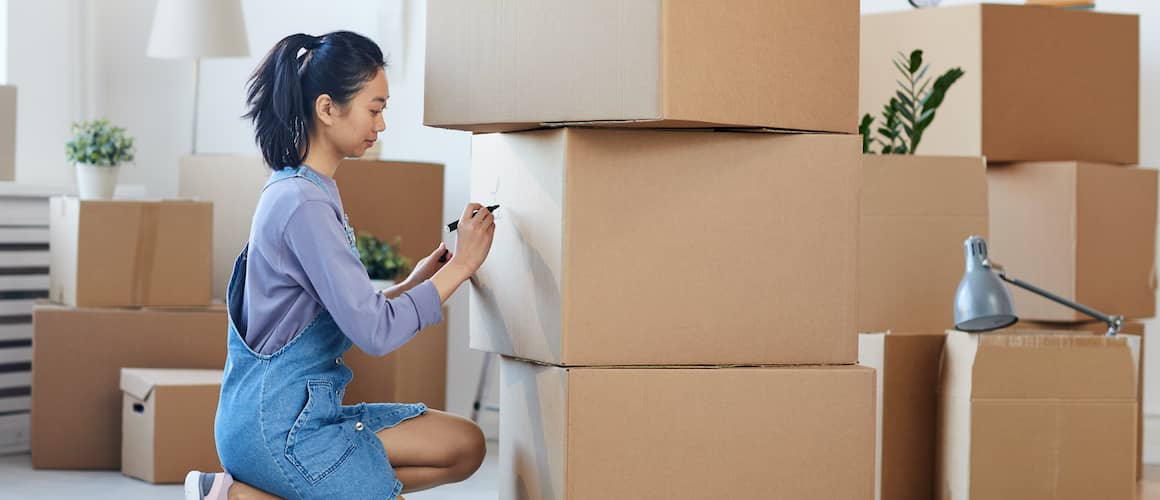 Woman writing on packing boxes, potentially depicting the process of packing or moving belongings.