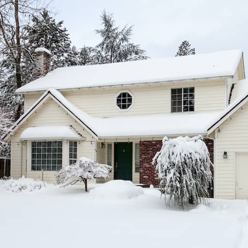 Two-story white house in winter with snowy lawn and trees.