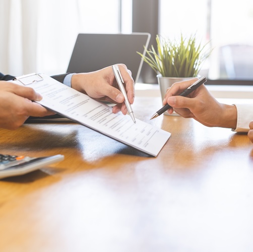 Close-up of someone's hands signing paperwork being shown to them across a table.