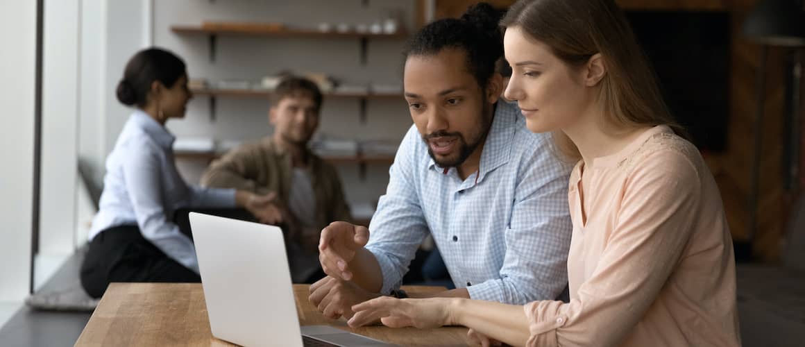 Male loan officer carefully explaining mortgage details on computer screen to engaged woman customer.