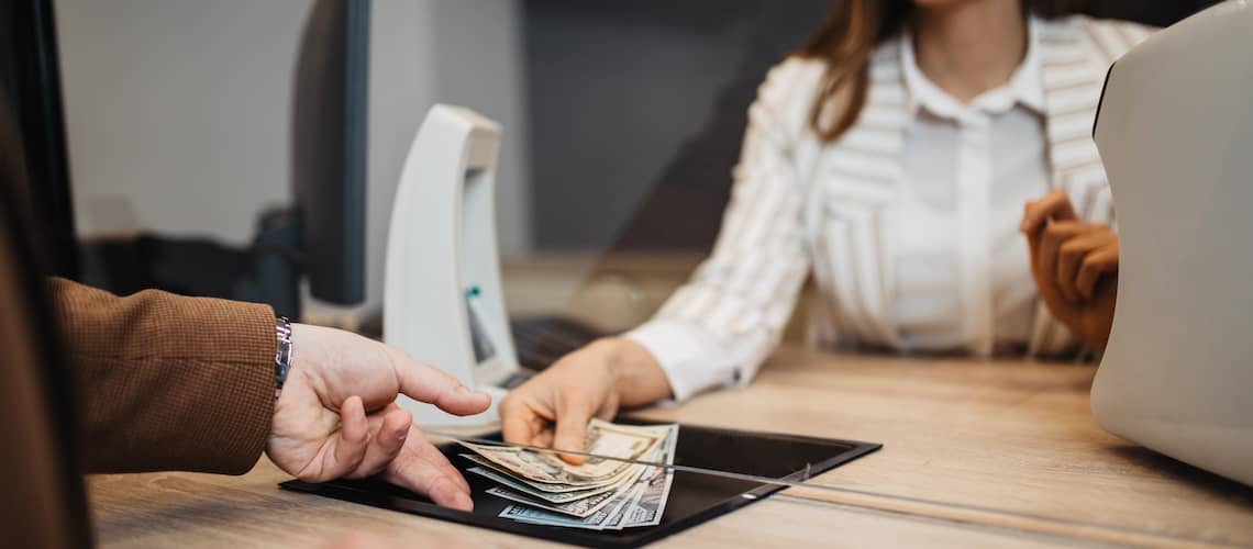 Female bankteller giving money to male customer at window.