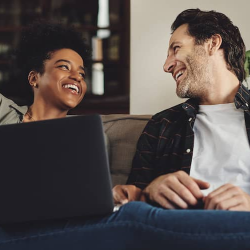 A couple on a couch with a laptop, potentially engaging in real estate-related activities or discussions.