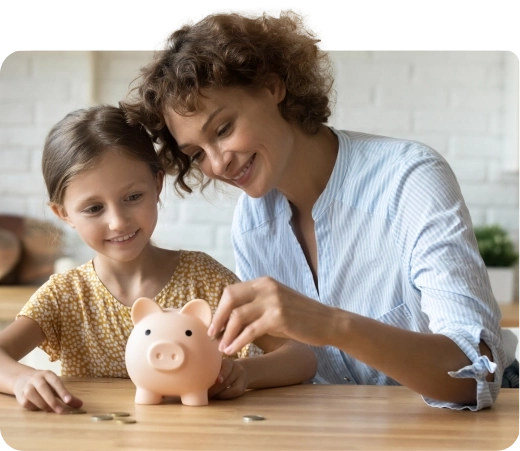 Woman and daughter sitting at a table putting money in a piggy bank.