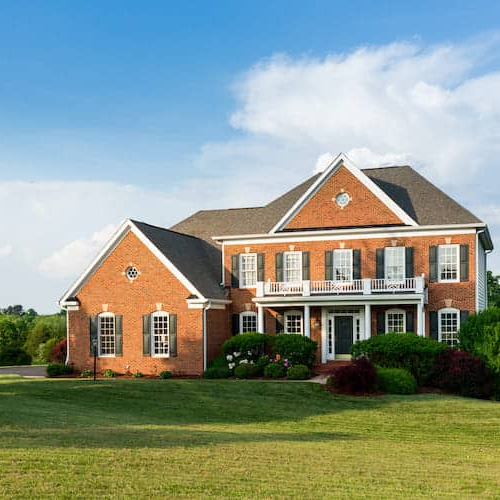 A large brick home with a sprawling green lawn and well-tended landscaping.