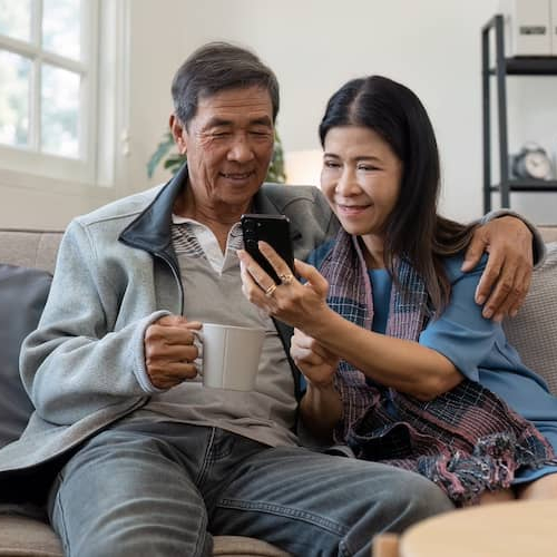 Older couple sitting on a couch together and looking at a cell phone.