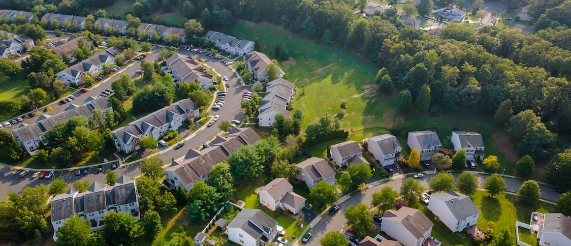 From above, a picturesque small town with neat streets, lined with colorful buildings and surrounded by greenery under a clear sky.