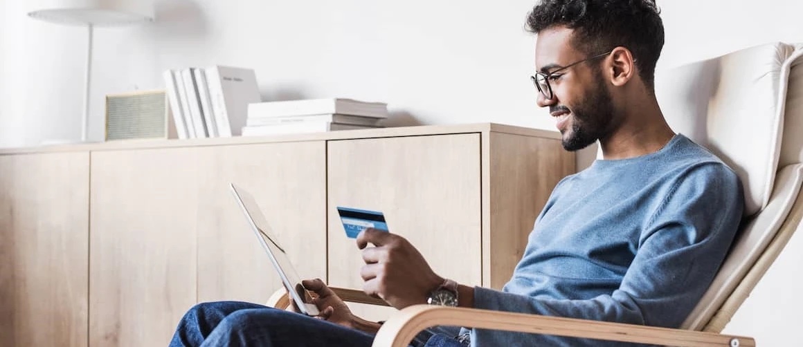 Man wearing glasses sitting in a chair and holding a credit card.