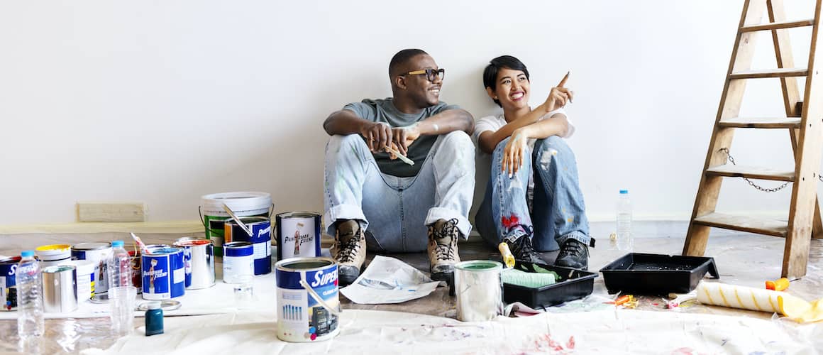 Couple sitting on floor with paint cans discussing home improvements.