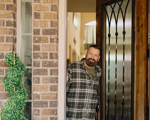 Man standing in doorway of brick house smiling.