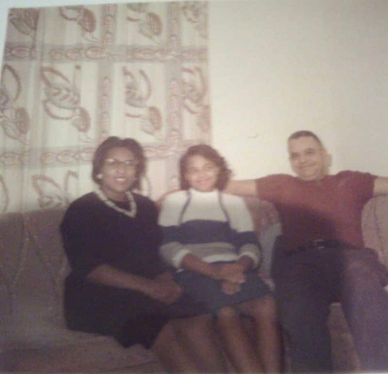 Young girl sits between a woman and a man on a couch, presumably her parents.