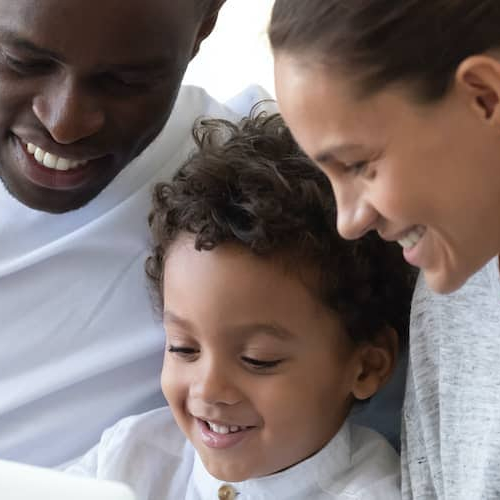Happy family gathered around laptop on couch enjoying their time.
