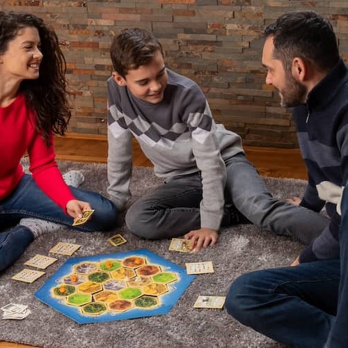 Small family of three playing a board game together, with a small dog nearby.