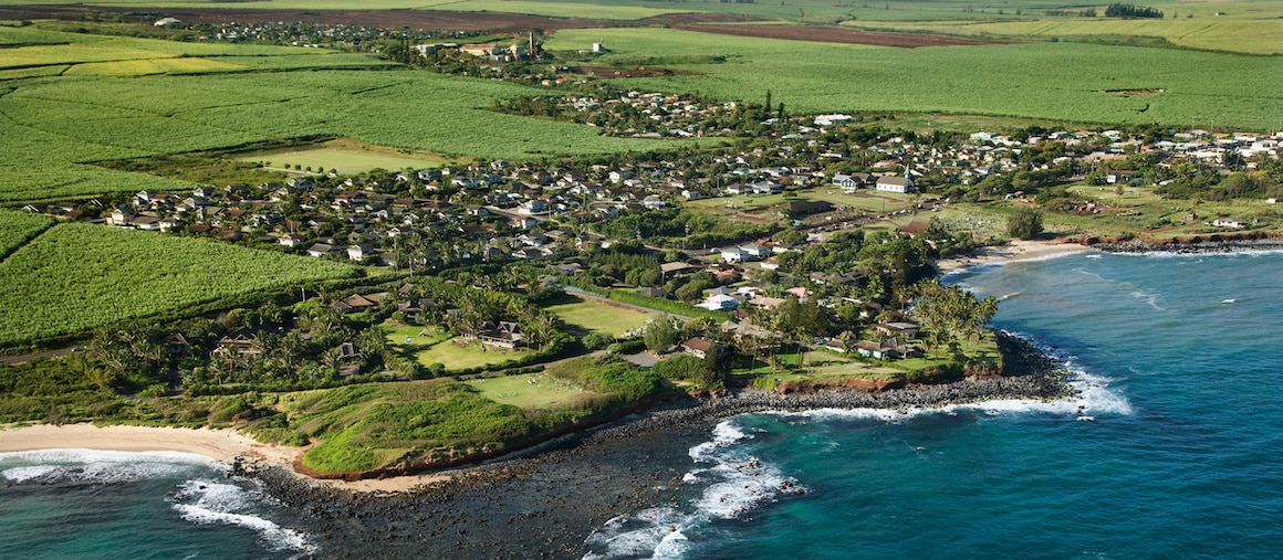 RHB Assets From IGX: A small town on the coastline of Hawaii with palm trees and the ocean in the background.